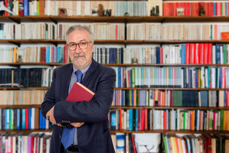 Stock: Male Professor Holding Book in Front of Bookcase